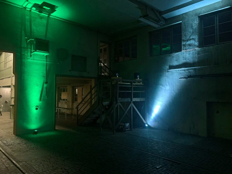 **Alt text:** Industrial event space illuminated with dramatic green and blue uplighting against textured concrete walls.
